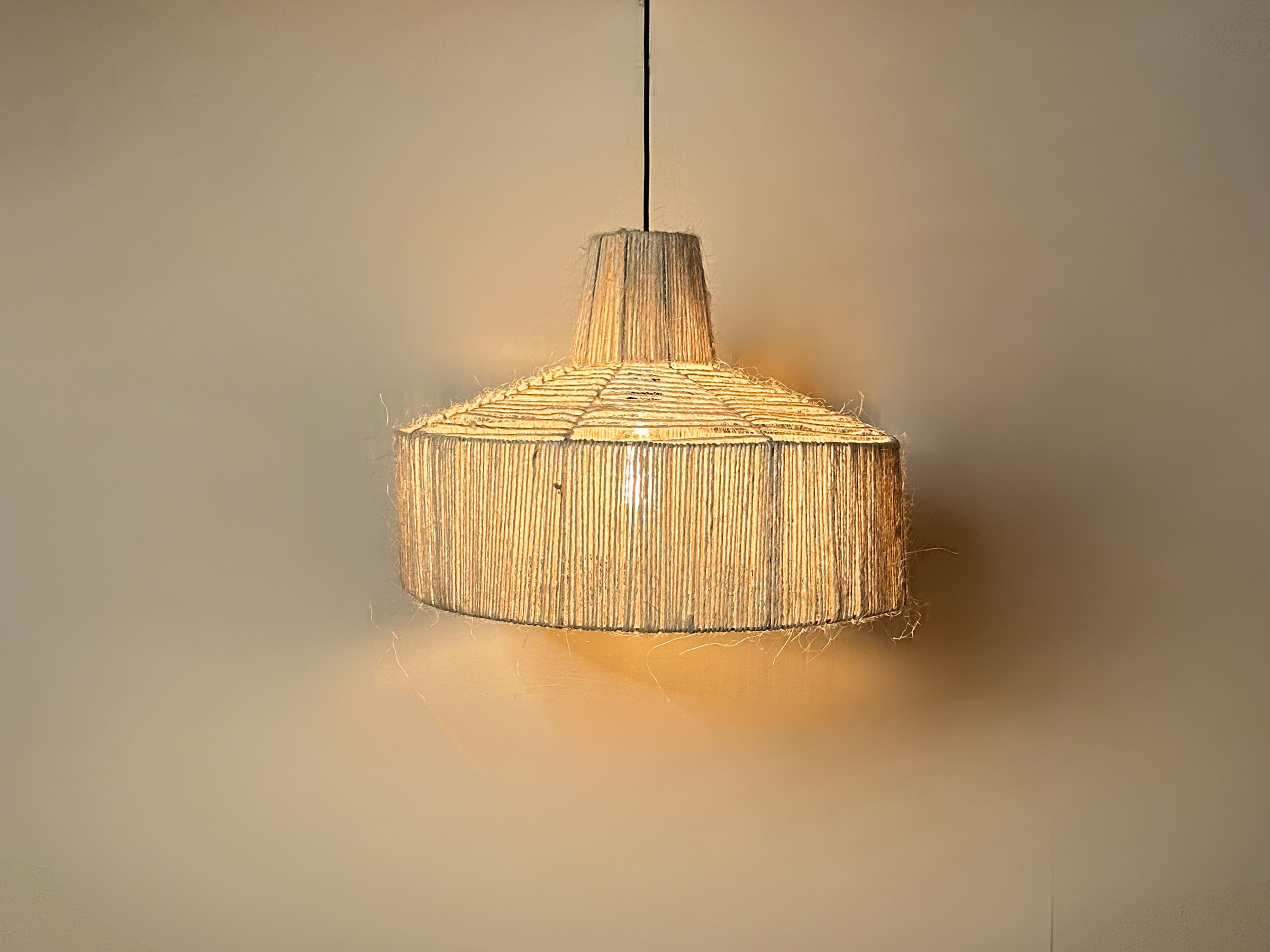 The Sisal pendant powered on in front of a wall