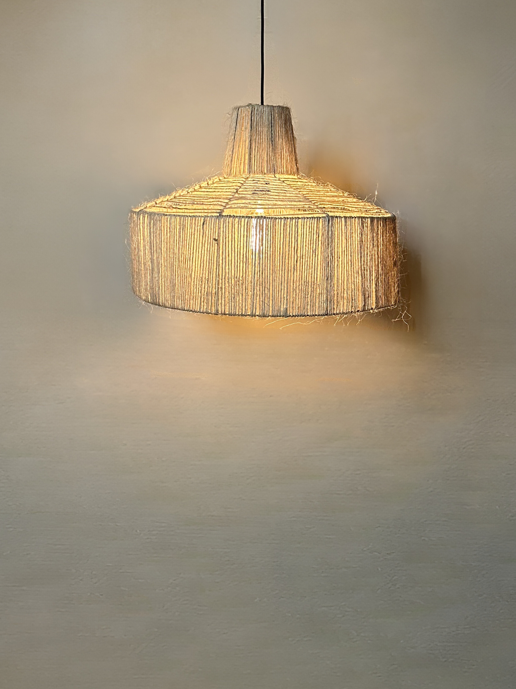 The Sisal pendant powered on in front of a wall