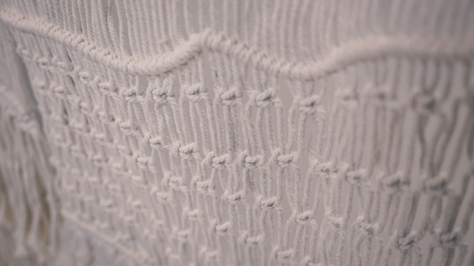 Load video: Close-up of the macrame wall hanger photographed against a neutral background showcasing the design