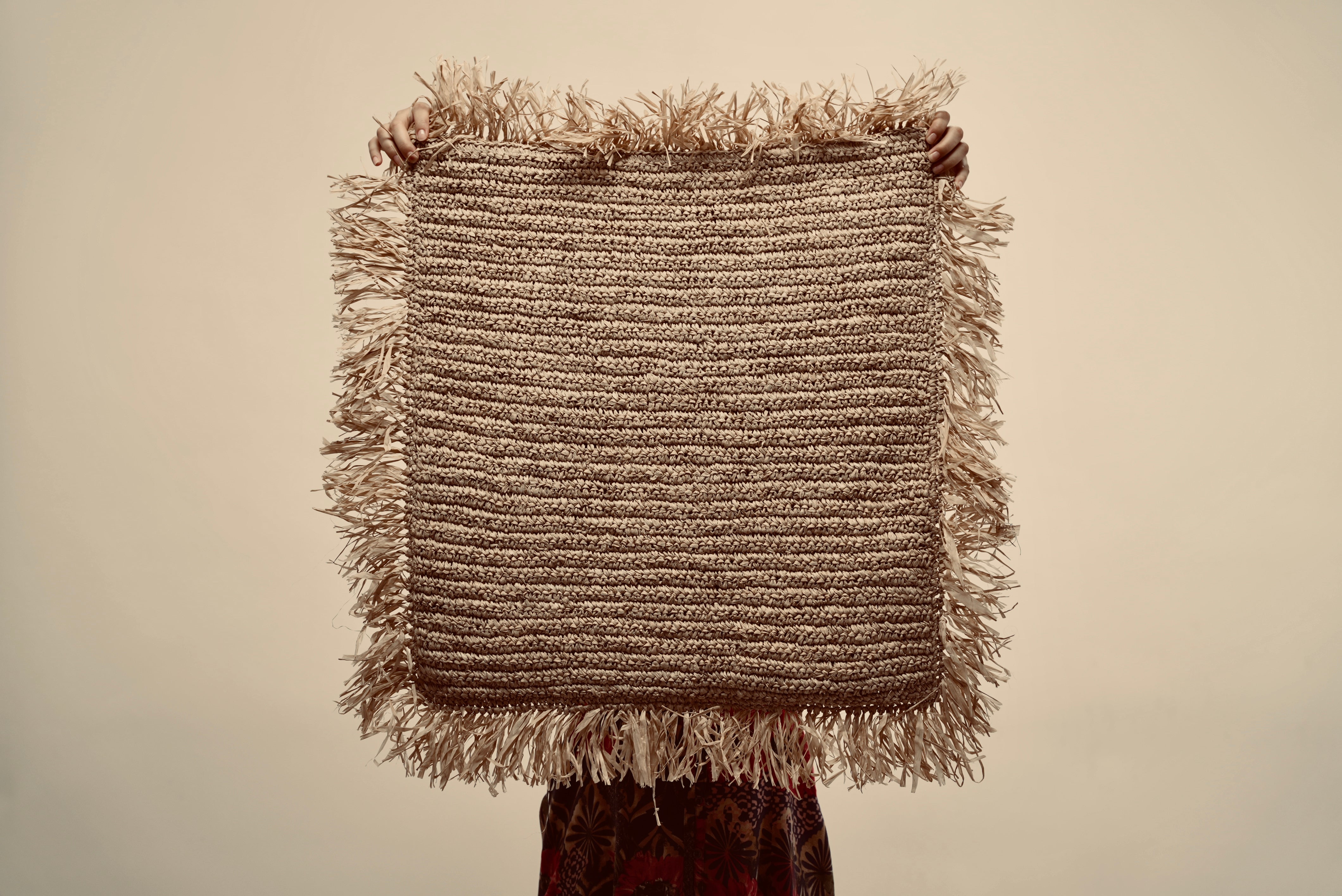 The Raffia cushion cover held up by a person to showcase the size of it
