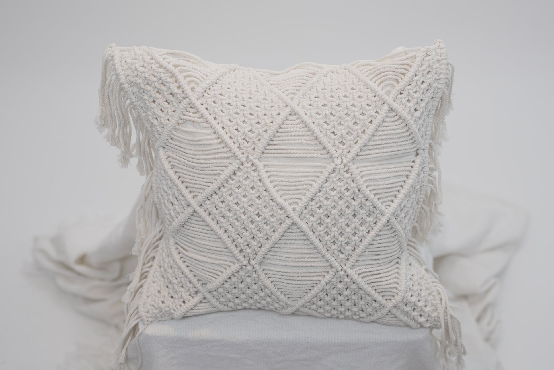A close-up of the macrame scatter cushions photographed against a neutral background
