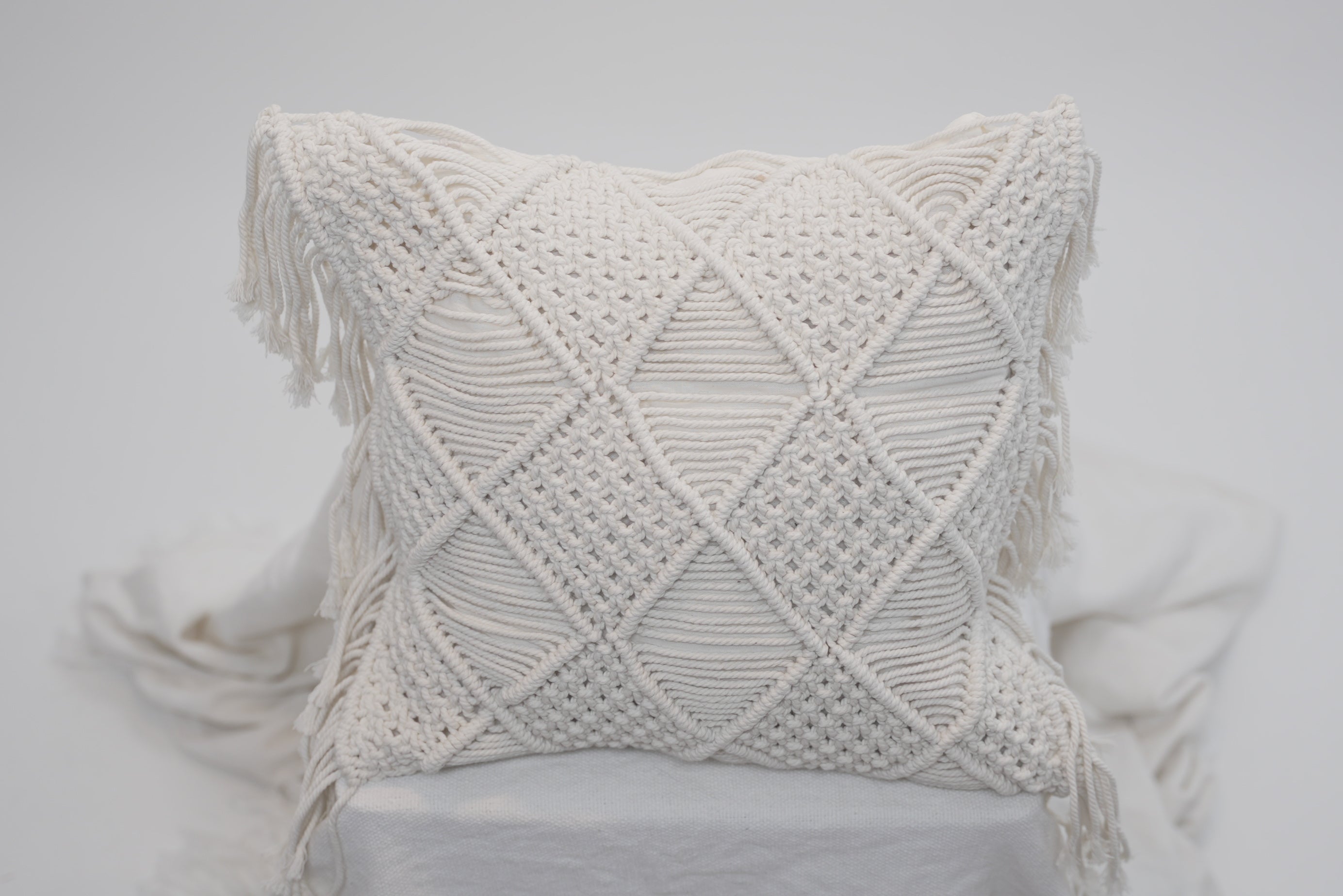A close-up of the macrame scatter cushions photographed against a neutral background