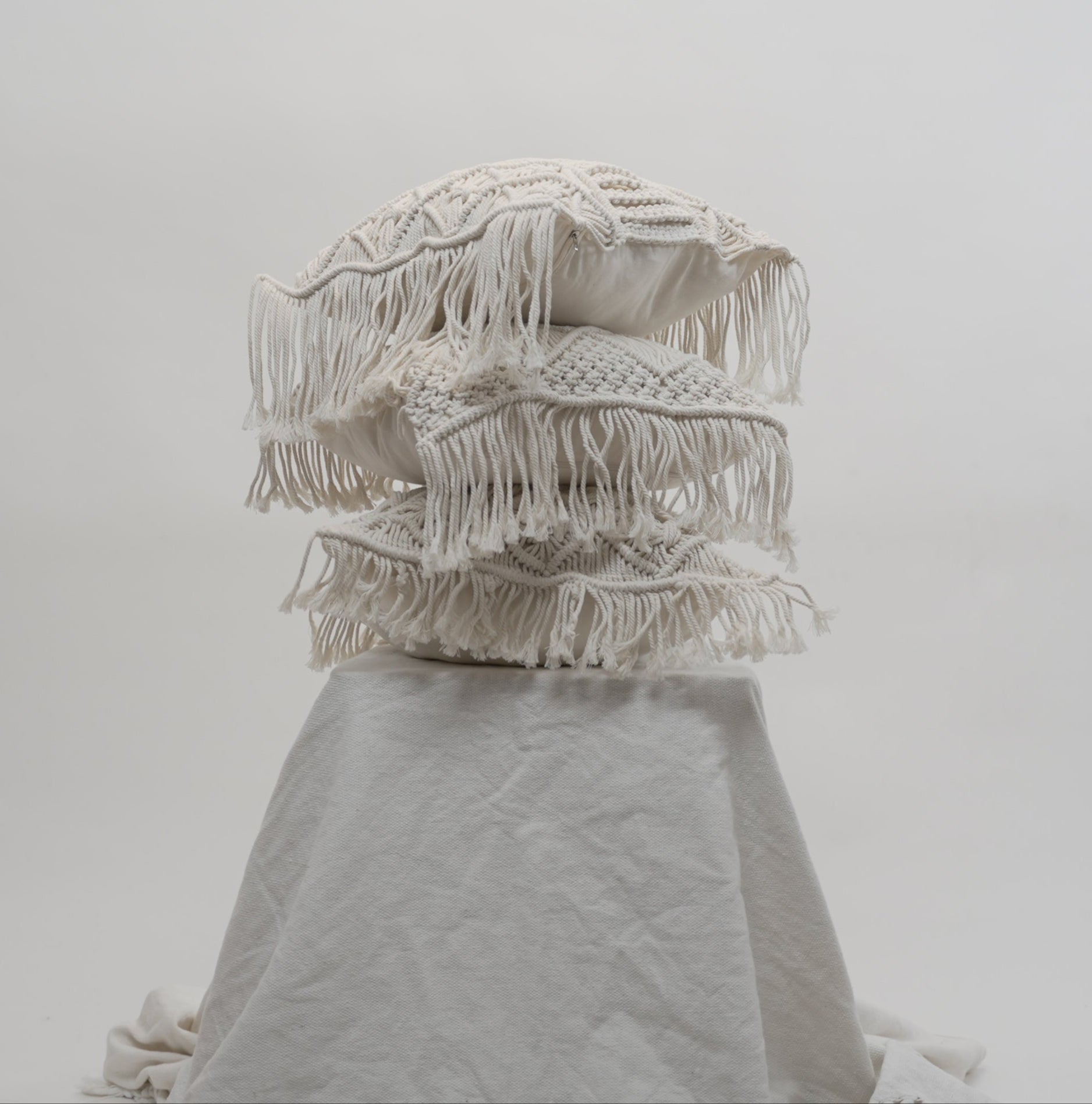 The macrame scatter cushions stacked on each other photographed against a neutral background