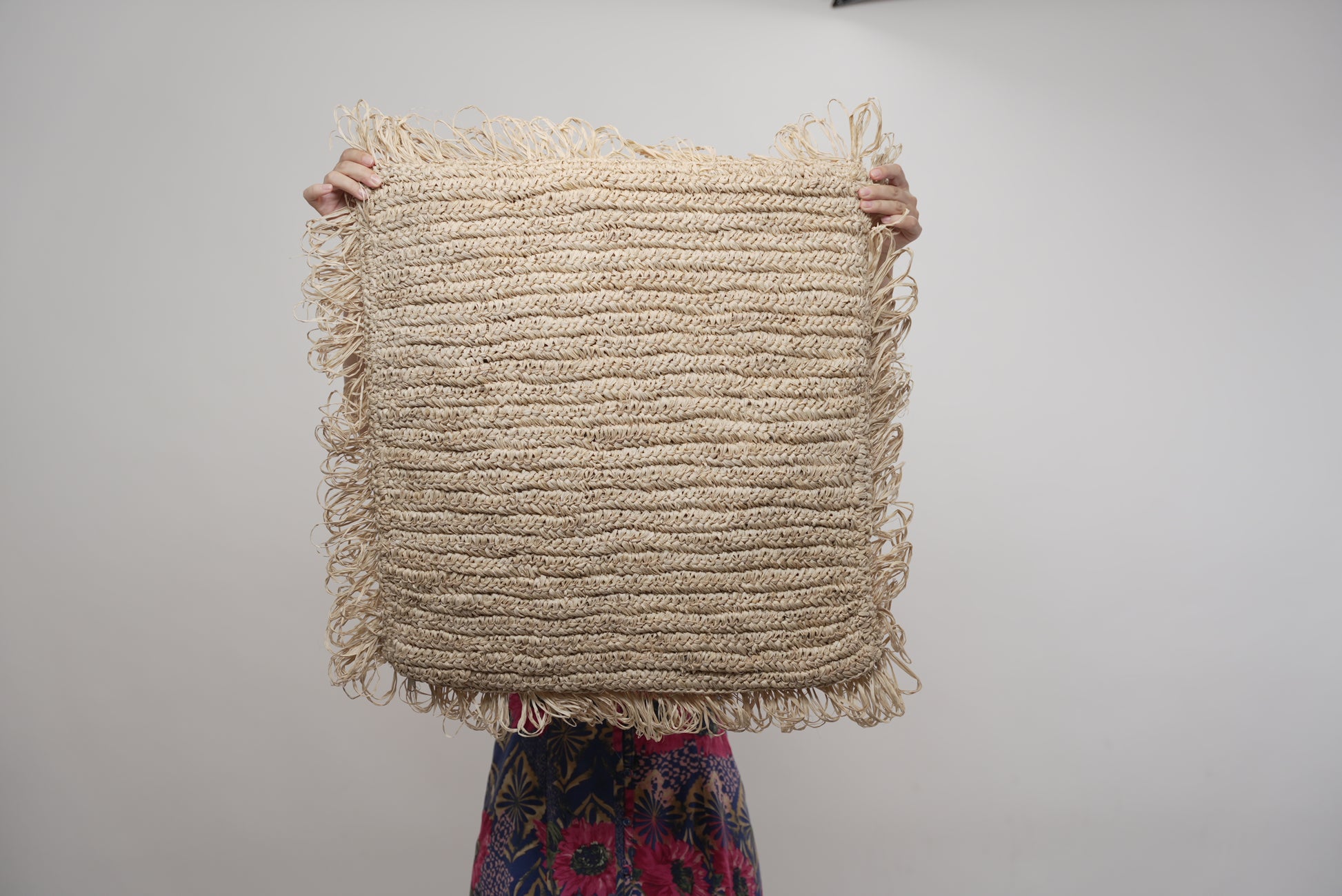 The Raffia cushion cover held up by a person to showcase the size of it