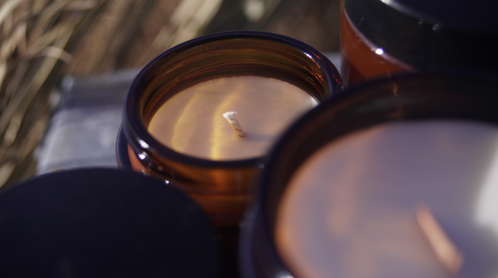Close-up of unlit soy candles in amber glass jars with cotton wicks, photographed in natural light.